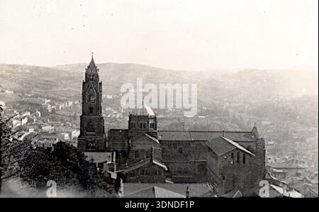 Im Zentrum der Kathedrale befindet sich ein Panoramablick auf Le Puy‑en‑Velay, der von einem hohen Kirchturm mit Kirchturm, einer großen Kuppel und mehrschichtigen Satteldächern geprägt ist. Dichte Gebäude klettern an den umliegenden Hängen und schaffen ein gestuftes urbanes Gewebe. Die Masse und die erhöhte Position des Doms verdichten die Szene im aufsteigenden Gelände der Stadt. Aus einer Sammlung einzigartiger Fotografien des 20. Jahrhunderts. Amateurfotograf, Schnappschüsse und einige größere in einem einzigen Album, das die Reisen einer Familie in Europa dokumentiert. Stockfoto