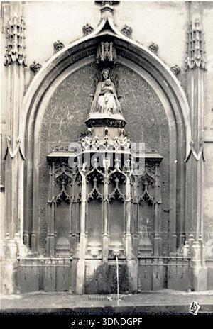 Eine gekrönte Figur steht unter einem kunstvollen gotischen Baldachin, eingerahmt von spitzen Bögen, schlanken Säulen und dichten Trazereien. Die Statue erhebt sich von einem reich verzierten Sockel, umgeben von Steinschnitzereien. Die vertikale Zugkraft und die komplizierten Details vermitteln den skulpturalen Reichtum, der für die Fassaden der Kathedrale von Rouen charakteristisch ist. Aus einer Sammlung einzigartiger Fotografien des 20. Jahrhunderts. Amateurfotograf, Schnappschüsse und einige größere in einem einzigen Album, das die Reisen einer Familie in Europa dokumentiert. Stockfoto