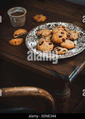 Hausgemachte Schokoladenchips-Cookies auf einem Teller und eine Tasse Kaffee auf einem rustikalen Tisch Stockfoto
