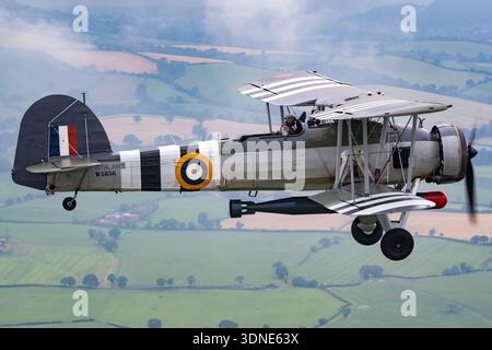 Luft-Luft-Nahaufnahme eines Fairey-Schwertfisch-Torpedobombers Mk I, Registrierung G-BMGC, abwechselnde Serie W5856, gezeigt in Royal Navy-Markierungen über Sleapkosh, Shropshire, 2024. Der Schwertfisch Mk I ist ein einmotoriger, dreisitziger Doppeldecker mit festem Fahrwerk und mit Stoff bedeckten Flügeln. Er wird von einem luftgekühlten Bristol Pegasus IIIM-9-Zylinder-Radialkolbenmotor angetrieben, der einen dreiflügeligen Propeller antreibt. Das Bild konzentriert sich auf den offenen Cockpit-Bereich, den vorderen Rumpf, die Motorverkleidung und die obere Flügelstruktur im Flug. Stockfoto