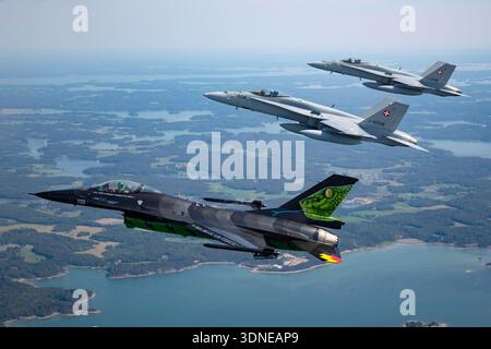 Eine belgische Luftwaffe F-16AM, die Falcon FA-87 mit Dream Viper Artwork kämpft, fliegt in enger Formation mit der Schweizer Luftwaffe F/A-18C Hornet auf der Turku Airshow 2023 in Finnland. Die F-16AM verfügt über einen einzelnen Pratt und Whitney F100-PW-220 Turbofan-Motor, während die F/A-18C Hornets von zwei General Electric F404-GE-402 Turboventilatoren angetrieben werden. Das Luft-Luft-Bild betont enge Formationsabstände, Cockpit-Details und den Kontrast zwischen Standard- und Speziallackierungen. Stockfoto