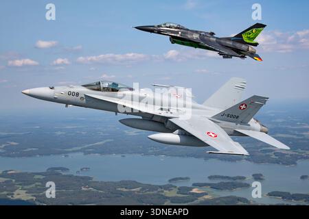 Die belgische F-16AM FA-87 und die Schweizer F/A-18C Hornet J-5008 führen Kunstflugmanöver auf der Turku Airshow 2023 durch. Beide Flugzeuge haben spezielle Lackierungen und Heckmarkierungen. Die F-16AM verfügt über einen Pratt & Whitney F100-PW-220 Turbofan, während die F/A-18C Hornet zwei General Electric F404-GE-402-Motoren hat. Die Bilder umfassen eine Nahaufnahme des Cockpits und der Luft-Luft-Ansicht, die Formationsflüge und Einzelflüge sowie die Manövrierfähigkeit und Leistungsfähigkeit des Flugzeugs zeigt. Stockfoto