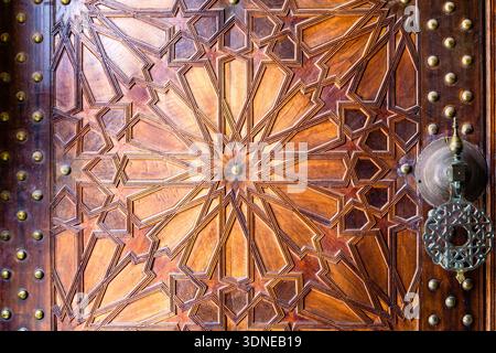 Eine wunderschön geschnitzte Holztür mit geometrischen Mustern und einem traditionellen Metallklopfer. Stockfoto