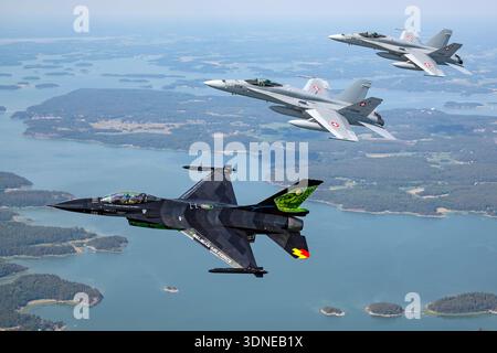 Ein belgischer Luftwaffe F-16AM kämpfender Falke in Dream Viper-Lackierung fliegt während der Turku Airshow 2023 in Finnland Luft zu Luft mit F/A-18C Hornet Flugzeugen der Schweizer Luftwaffe. Der F-16AM wird von einem einzelnen Pratt und Whitney F100-PW-220 Turbofan-Motor angetrieben. Die F/A-18C Hornissen sind mit zwei General Electric F404-GE-402 Turboventilatoren ausgestattet. Das Bild zeigt Details aus dem Cockpit, nationale Abzeichen, Heckkunst und koordinierte Kunstflugmanöver. Stockfoto