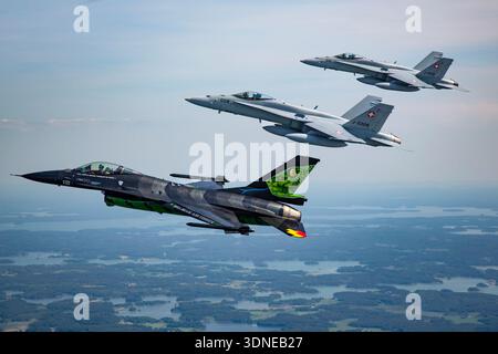 Die belgische Luftwaffe F-16AM kämpfte Falcon FA-87 und die Schweizer Luftwaffe F/A-18C Hornet fliegen während einer Kunstflugsequenz auf der Turku Airshow 2023 in Finnland in einer engen Formation. Die F-16AM ist ein einmotoriger Mehrzweckjäger, der von einem Pratt und Whitney F100-PW-220 Turbofan angetrieben wird. Die F/A-18C Hornets sind zweimotorige Düsen mit General Electric F404-GE-402 Turboventilatoren. Die Luft-Luft-Ansicht zeigt Cockpit-Bereiche, spezielle Lackierungen und diszipliniertes Formationsfliegen. Stockfoto