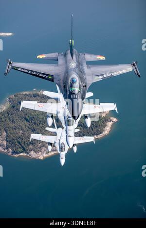 Das Bild zeigt eine belgische Luftwaffe F-16AM, die die Falcon FA-87 in Dream Viper-Lackierung ankämpft, die während der Flugschau 2023 in Finnland mit der Schweizer Luftwaffe F/A-18C Hornet über Turku flog. Die F-16AM ist ein leichtes einmotoriges Kampfflugzeug mit Pratt und Whitney F100-PW-220 Turbofan. Die F/A-18C Hornet ist ein trägerfähiges zweimotoriges Mehrzweckflugzeug, das von zwei General Electric F404-GE-402 Turboventilatoren angetrieben wird. Die Überkopfperspektive betont Formation Kunstflug, nationale Markierungen und spezielle Displayfarben. Stockfoto
