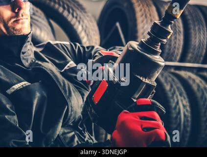 Ein Arbeiter trägt Handschuhe und verwendet ein Werkzeug, während er in einer Werkstatt von Reifen umgeben ist. Stockfoto