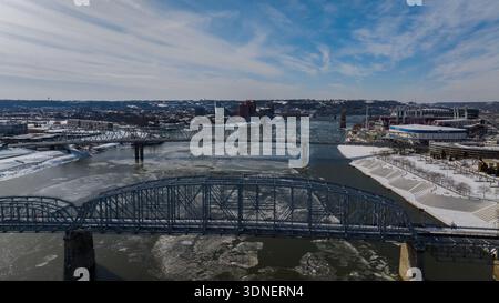 Blick aus der Vogelperspektive auf Brücken über dem eisigen Fluss, die den hellen Winterhimmel reflektieren, mit dem Great American Ball Park und dem Paycor Stadium in der Ferne, Cincinnati Stockfoto