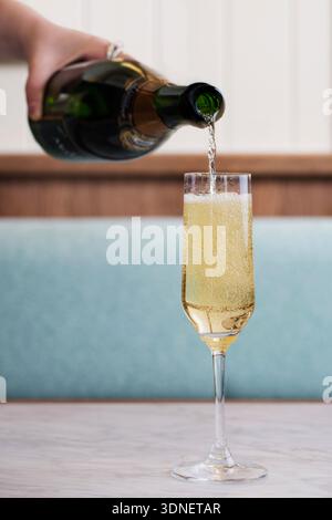 Sekt in eine Champagnerflöte gegossen, goldene Seifenblasen steigen in sanftem natürlichem Licht auf, intimer Feierabend. Stockfoto