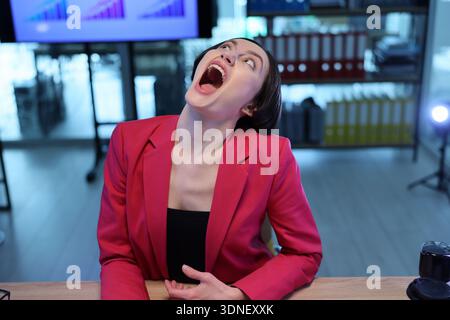 Frau in einem leuchtend rosa Blazer drückt überwältigende Freude während eines lebhaften Geschäftstreffens in einem modernen Büroumfeld aus Stockfoto