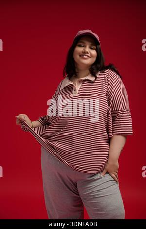 Das Modell in Übergröße strahlt Vertrauen aus in einem trendigen gestreiften Oberteil und einer sportlichen Cap, die fröhlich posiert. Stockfoto