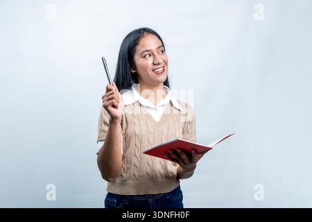 Eine junge indonesische Frau, die auf einem Stuhl sitzt und ihr Smartphone hält, während sie mit einem fröhlichen und freundlichen Lächeln in die Kamera blickt. Stockfoto