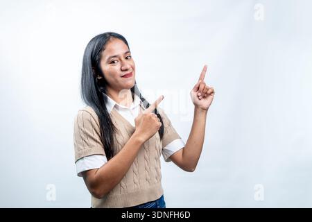 Eine glückliche junge indonesische Frau, die ihre Finger nach oben und zur Seite zeigt und leere Flächen für Text, Werbung oder Produktplatzierung bietet. Stockfoto