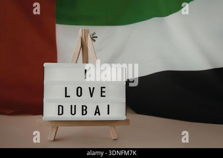 Ein Schild auf einer Staffelei mit der Aufschrift „I love Dubai“ vor der Flagge der Vereinigten Arabischen Emirate. Stockfoto