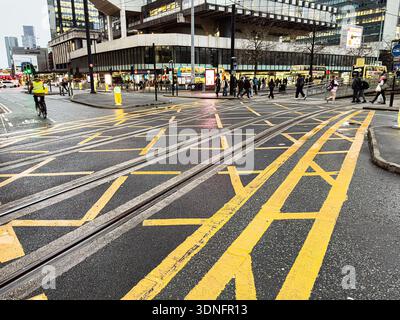 Manchester, Großbritannien - 22. Januar 2026: Stadtszene in Manchester mit Straßenbahnlinien, Fußgängern und gelben Straßenmarkierungen. Stockfoto