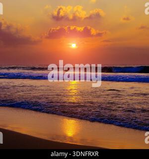 Wunderschöner Sonnenuntergang über Meer oder Meer. Lebendige und weiche Farben, magisches Licht. Kleine Wolken am Himmel, Spiegelung der Sonne im Wasser und Sand am Strand. Stockfoto