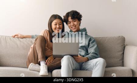 Paare sitzen auf dem Sofa und teilen sich Momente, während sie gemeinsam im Wohnzimmer auf den Laptop schauen Stockfoto