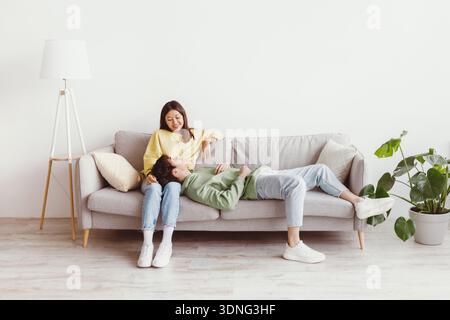 Gemeinsame Freizeit. Glückliches junges asiatisches Paar, das zusammen ein Wochenende verbringt, sich zu Hause auf der Couch ausruht und Platz kopiert Stockfoto