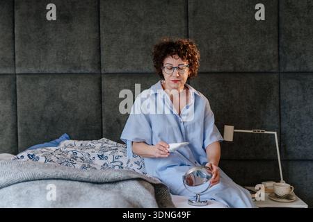 Reife Frau liest Buch und streichelt weiße Katze in gemütlichen Wohnzimmer Sessel Home Relaxation Stockfoto