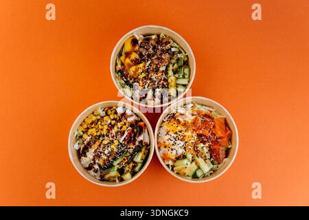 Drei Poke Schüsseln mit Reis, Lachs, Tofu und Gemüse auf orangem Hintergrund Stockfoto