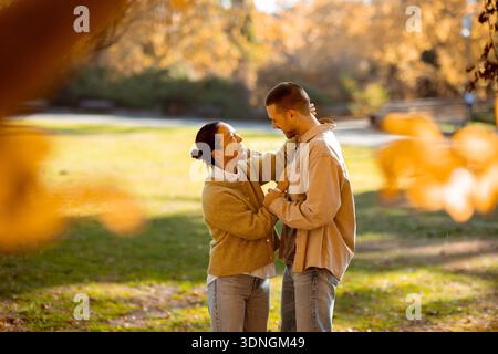 In einem hellen Herbstpark teilen sich eine Koreanerin und ein Kaukasier Lächeln, lachen und genießen ihre gemeinsame Zeit inmitten fallender Blätter. Stockfoto