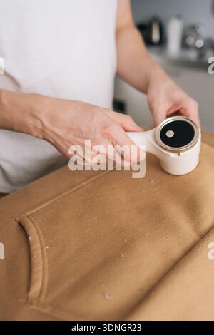 Vertikaler Schnitt einer Person mit elektrischem Stoffrasierer, Entfernung von Pilling und Fuzz vom Sweatshirt, Erhaltung des Erscheinungsbildes der Kleidung und des Textils Stockfoto