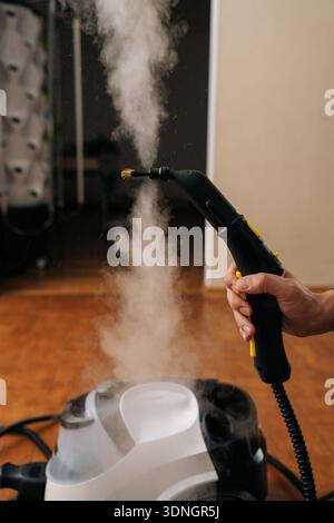 Vertikal geschnittener Schuss eines nicht erkennbaren Mannes mit Dampfreinigungsmaschine, der starken heißen Dampf für eine effektive Hygiene und Tiefenreinigung freisetzt Stockfoto