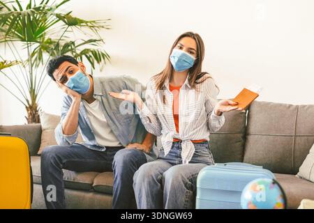 Verärgertes Touristenpaar nach der Absage der Tour auf dem Sofa mit Koffern und Fahrkarten sitzen Stockfoto