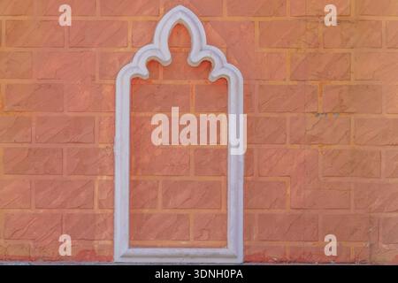 Ein dekoratives weißes Bogendesign, eingebettet in eine orangene Ziegelwand, die einen traditionellen architektonischen Rahmen schafft. Stockfoto