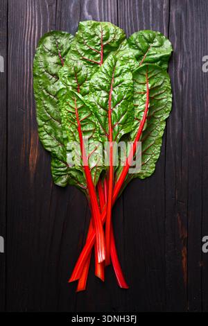 Frische Mangold-Blätter mit roten Stielen, flach auf rustikalem Holz gelegt. Gesundes Bio-Grünkonzept Stockfoto