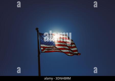Die Flagge der Vereinigten Staaten flattert auf einem Pfosten unter der hellen Mittagssonne. Der blaue Himmel dient als Hintergrund und betont die Farben und das Design von Stockfoto