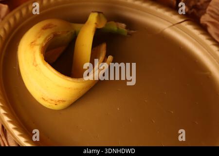 Eine Bananenschale liegt auf einem braunen Teller auf einem Tisch, der mit Stoff bedeckt ist. Die Einstellung zeigt eine einfache Wohnumgebung mit sanftem Tageslicht Stockfoto