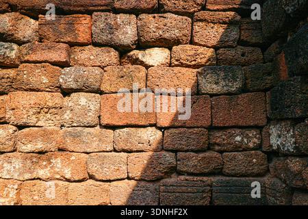 Sonnendurchflutete Lateritsteinwand mit scharfem diagonalem Schatten für minimalistische architektonische Textur in warmen roten braunen Erdtönen. Stockfoto