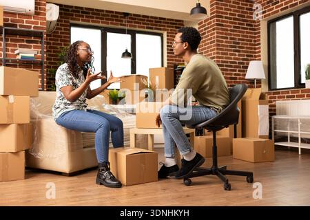 Schwarz verheiratete Paare haben angespannte Momente, streiten sich drinnen, umgeben von Paketen. afroamerikanische Freundin und Freund in hitziger Diskussion, was den Stress widerspiegelt, in ein neues Zuhause umzuziehen. Stockfoto
