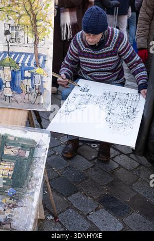 Paris, Frankreich; Dezember 30 2025: Ein älterer Straßenkünstler zeichnet auf dem Montmartre-Kunstmarkt ein Pariser Stadtbild auf Papier. Nahaufnahme des Malers bei der Arbeit Stockfoto