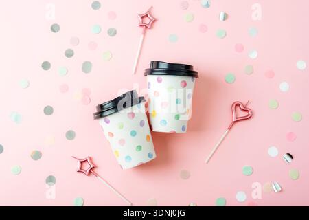 Zwei Kaffeetassen aus Papier mit Deckeln auf rosa Hintergrund mit Konfetti und Geburtstagskerzen. Draufsicht, flach Stockfoto