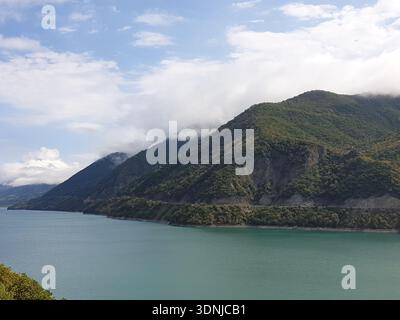 Ein Panoramablick auf das türkisfarbene Wasser des Zhinvali Reservoir, umgeben von üppigen grünen Bergen unter einem weichen, bewölkten Himmel in Georgien Stockfoto