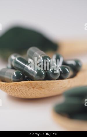 Spirulina-Kapseln auf einem Holzlöffel in einfacher Umgebung Stockfoto