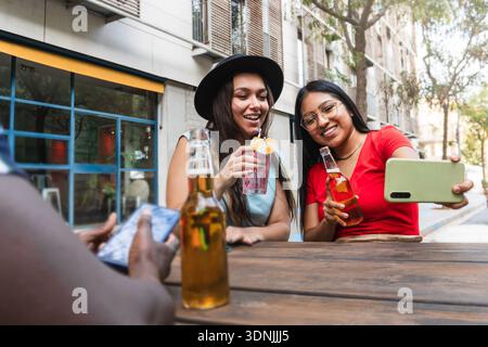 Gruppe von Freunden trinkt Bier und Cocktails auf der Stadterrasse - Junge glückliche Frauen, die Spaß beim Selfie im Freien haben - Millennial Sommer Urban Lifestyle Stockfoto