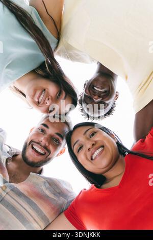 Glückliche multirassische Studenten umarmen sich im Kreis stehend und lächelnd in die Kamera - Freundschaft und Vielfalt Konzept - Niedrigwinkelansicht Stockfoto