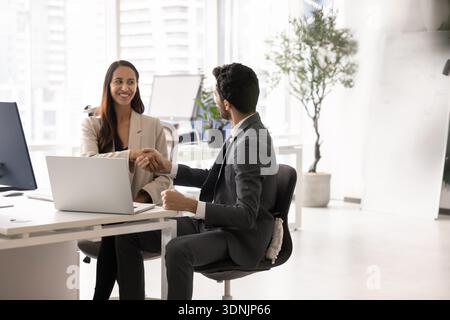 Kollegen sitzen mit Laptop am Tisch, schütteln die Hände und beenden das Meeting Stockfoto