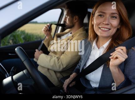 Eine Frau auf dem Fahrersitz und ein Mann auf dem Beifahrersitz, der die Sicherheitsgurte anschnallt, um die Sicherheit während der Fahrt zu demonstrieren Stockfoto