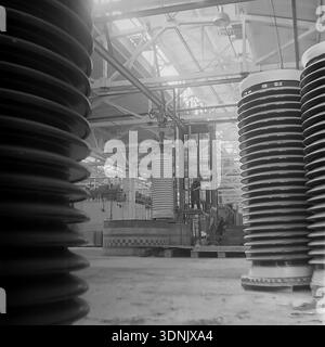 Slawjansk, Ukrainische SSR, 1960er Jahre Ein Archivfoto, das einen dramatischen Blick auf das Innere der Slawjansk Hochspannungs-Isolatoren-Anlage (ZVI) zeigt. Die zentrale Szene mit Arbeitern und einem Gabelstapler wird von massiven Keramikisolatoren im Vordergrund eingerahmt. Durch die Dachfenster des Werks strömt helles Licht und beleuchtet die riesige Produktionshalle im Donezk-Gebiet. Dieses Bild fängt perfekt die Schnittmenge von industrieller Arbeit, monumentalem Maßstab und der wirtschaftlichen Macht des friedlichen Donbass während des Höhepunkts der sowjetischen Industrialisierung ein. Stockfoto