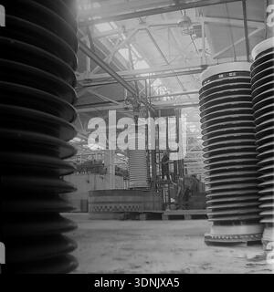 Slawjansk, Ukrainische SSR, 1960er Jahre Ein Archivfoto, das einen dramatischen Blick auf das Innere der Slawjansk Hochspannungs-Isolatoren-Anlage (ZVI) zeigt. Die zentrale Szene mit Arbeitern und einem Gabelstapler wird von massiven Keramikisolatoren im Vordergrund eingerahmt. Durch die Dachfenster des Werks strömt helles Licht und beleuchtet die riesige Produktionshalle im Donezk-Gebiet. Dieses Bild fängt perfekt die Schnittmenge von industrieller Arbeit, monumentalem Maßstab und der wirtschaftlichen Macht des friedlichen Donbass während des Höhepunkts der sowjetischen Industrialisierung ein. Stockfoto
