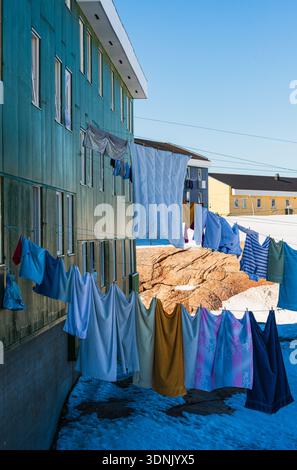Die Leute trocknen Wäsche vor ihren Wohnungen in Ilulissat, Grönland. Buntes Tuch hängt an den Linien zwischen Gebäuden. Schnee bedeckt das Gras Stockfoto