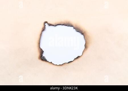 Verbranntes Loch in altem Papierbogen auf weißem Hintergrund, Nahaufnahme Stockfoto