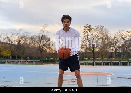 Junger Mann, der Basketball auf einem Freiluftplatz hält, fokussiertes Training, das Fitness, Können und entschlossene sportliche Energie betont Stockfoto