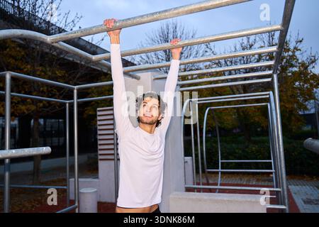 Sportlicher Mann, der an Bars im Freien trainiert, ein Ganzkörpertraining in einem städtischen Calisthenics-Park durchführt Stockfoto