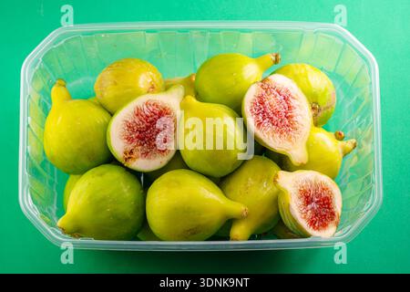 Reife grüne Feigenfrüchte in Kunststoffkiste, Draufsicht isoliert auf grünem Hintergrund. Stockfoto