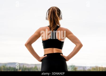 Sportliche Athletin im Kopfhörer, die sich nach dem Training im Freien ausruhen und den Horizont betrachten Stockfoto